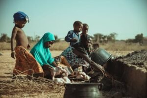 African family engaged in daily chores with traditional clothing in a rural setting.
